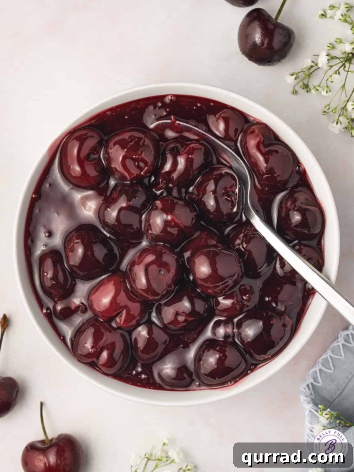 Overhead view of a bowl of glossy, vibrant red cherry pie filling, garnished with a few fresh cherries.