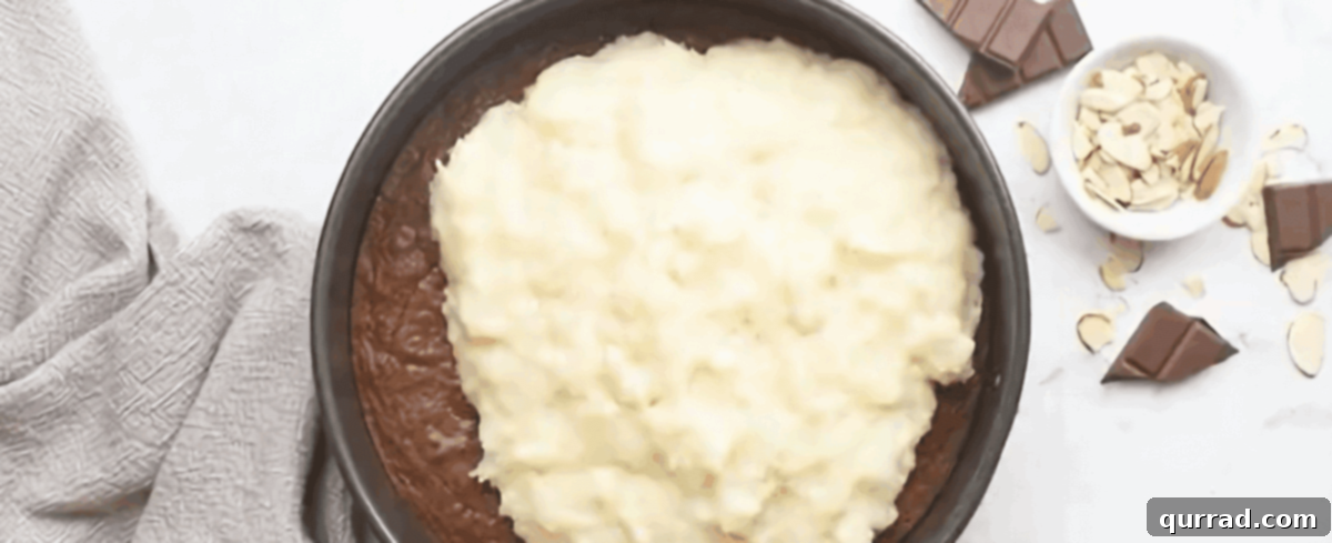 Carefully pouring the smooth coconut mixture over the baked brownie base.