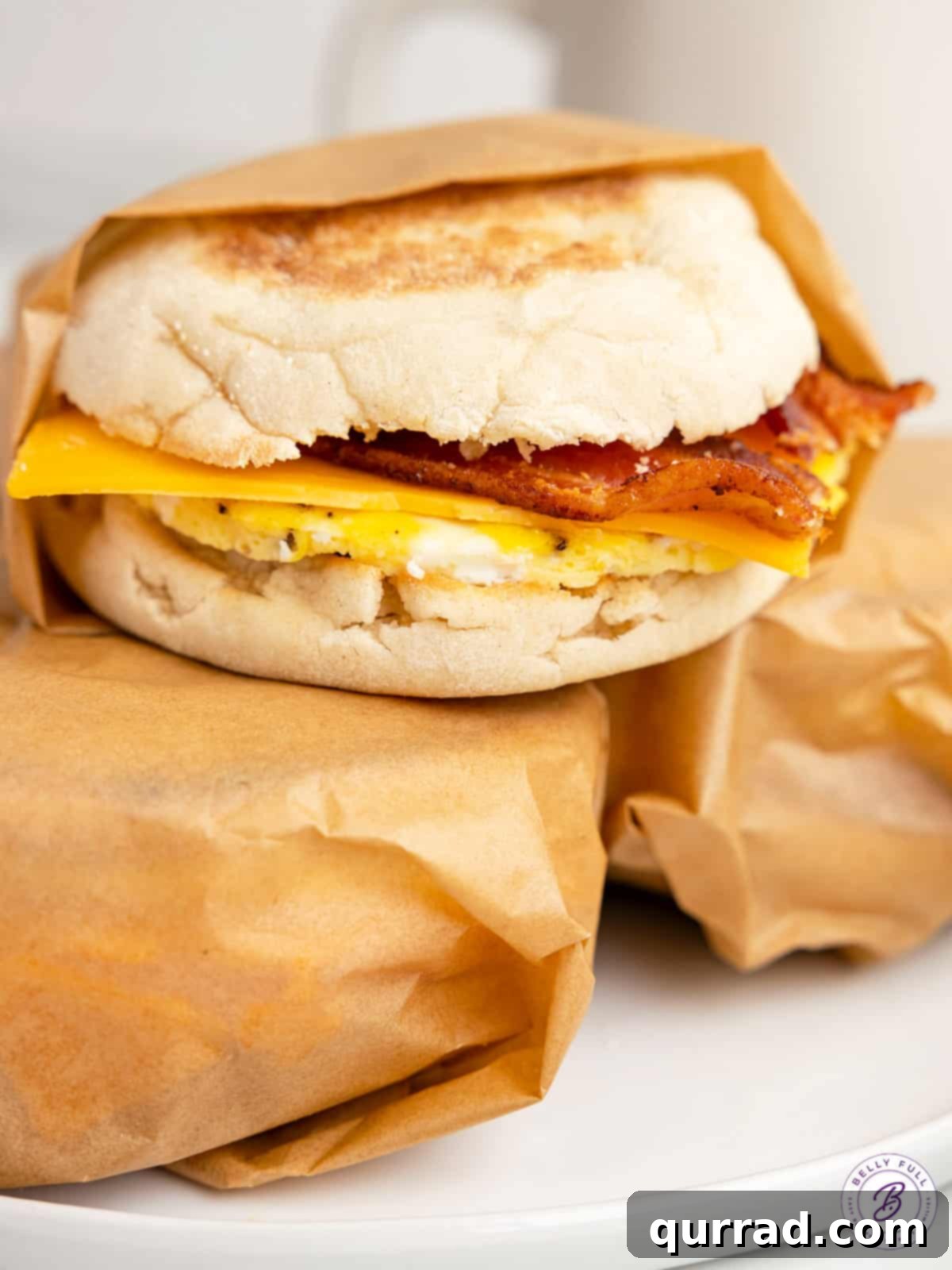 Made with egg, cheese, and breakfast meat on an English muffin, these Freezer Breakfast Sandwiches are perfect for busy mornings. Three make ahead breakfast sandwiches, two wrapped in parchment paper, showing the finished product.