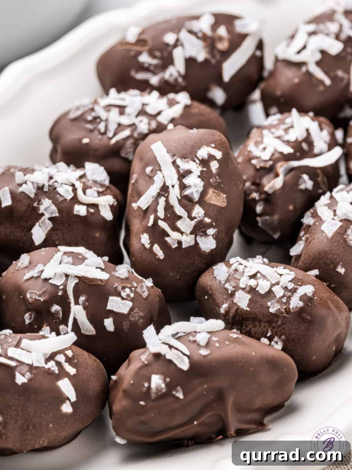 These healthy Almond Stuffed Dates taste exactly like the Almond Joy candy bar, making them an ideal guilt-free snack or dessert. Close-up of chocolate-covered dates, generously adorned with coconut, nestled on a parchment-lined tray, ready to be enjoyed.