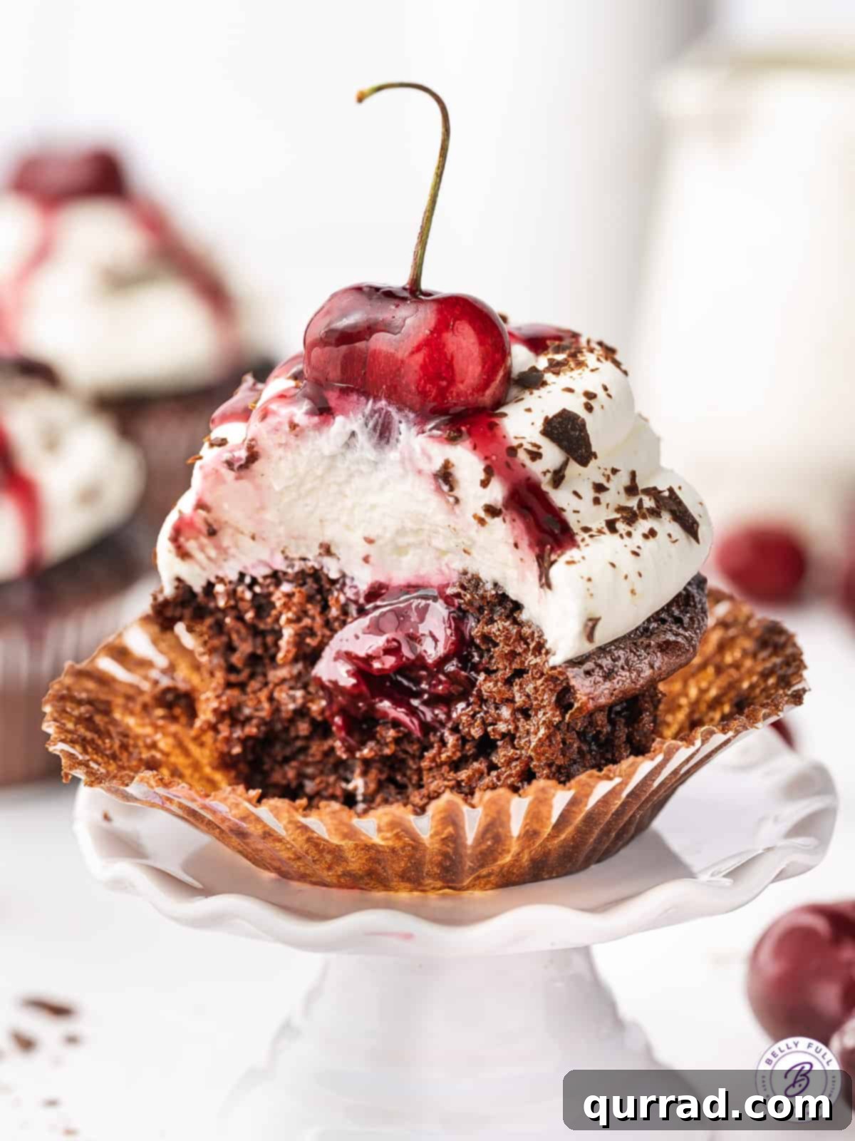 A black forest cupcake cut in half to show the cherry filling