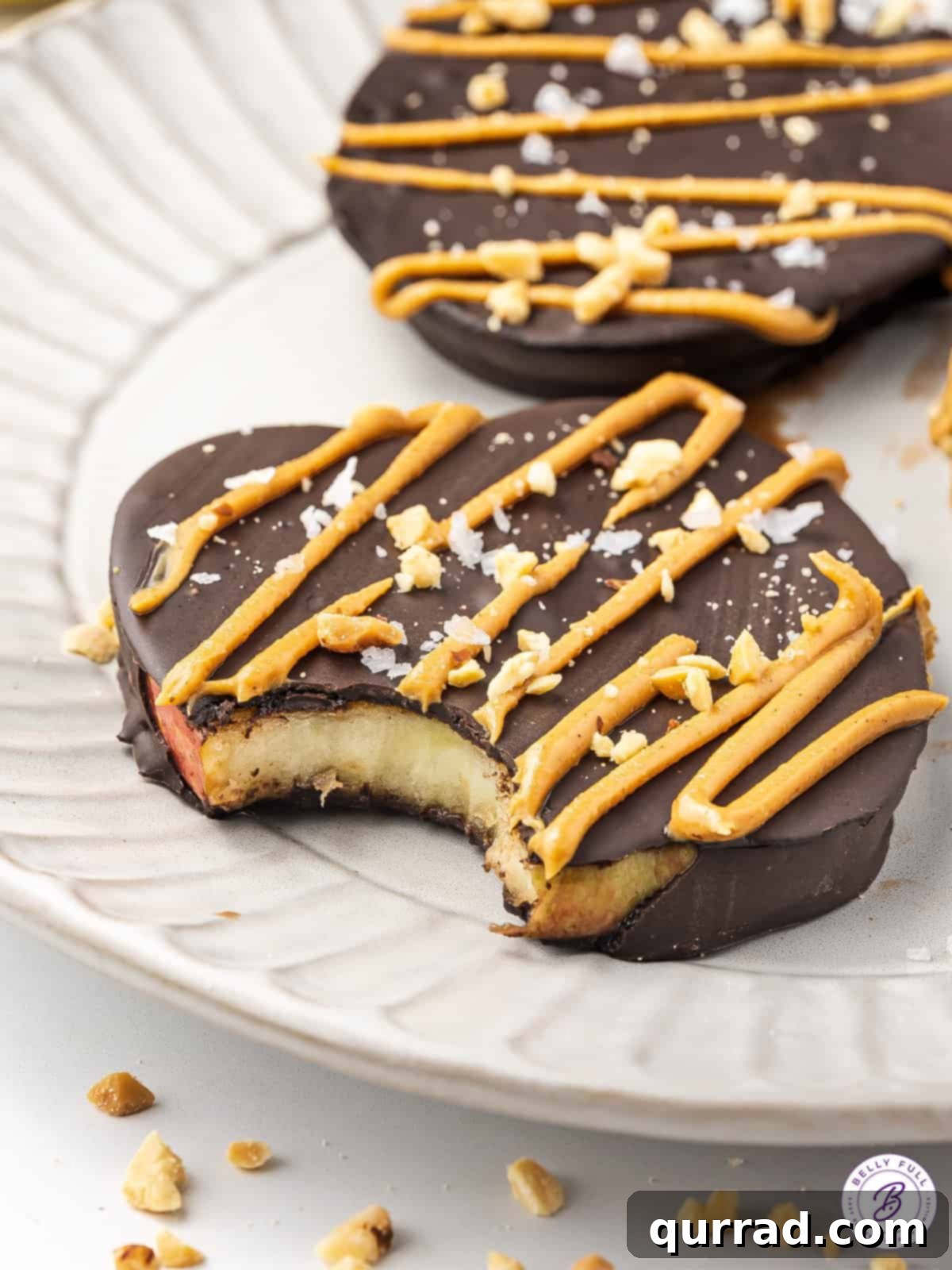 Two chocolate dipped apple slices on a plate, one with a bite taken out, showing the crisp apple inside