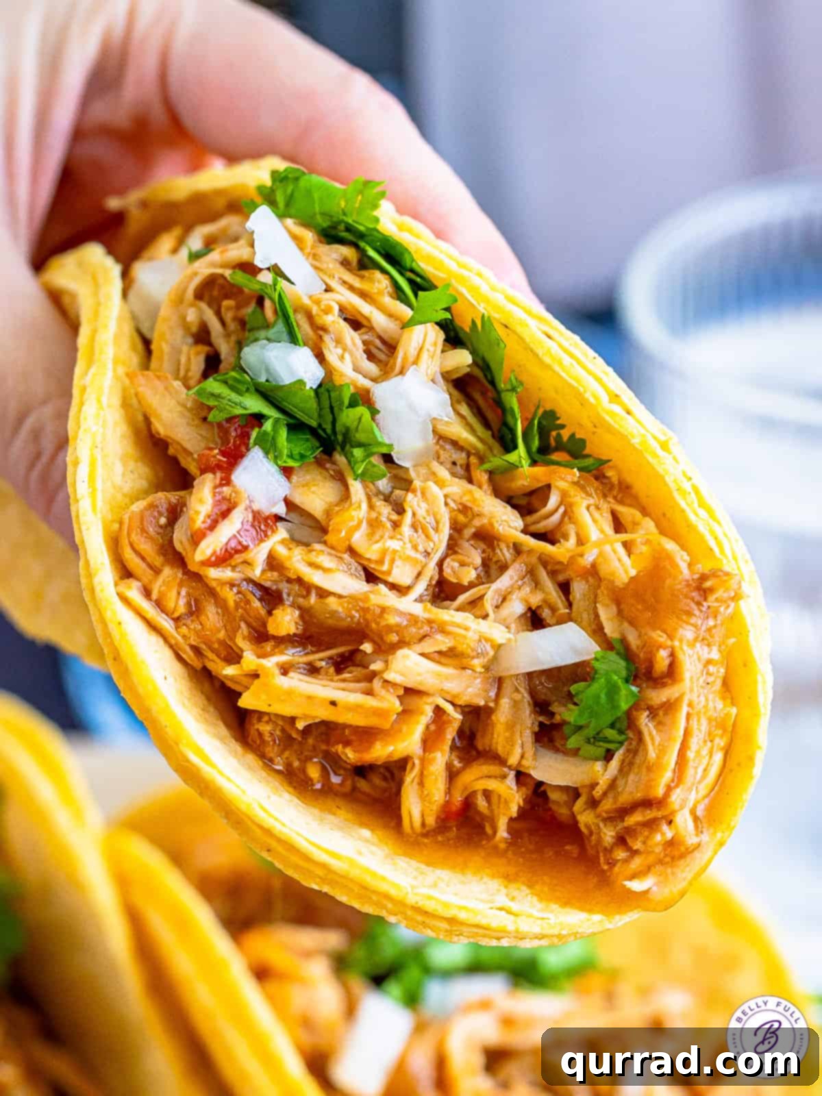 A hand holding a shredded chicken taco, showcasing the tender chicken and fresh toppings.