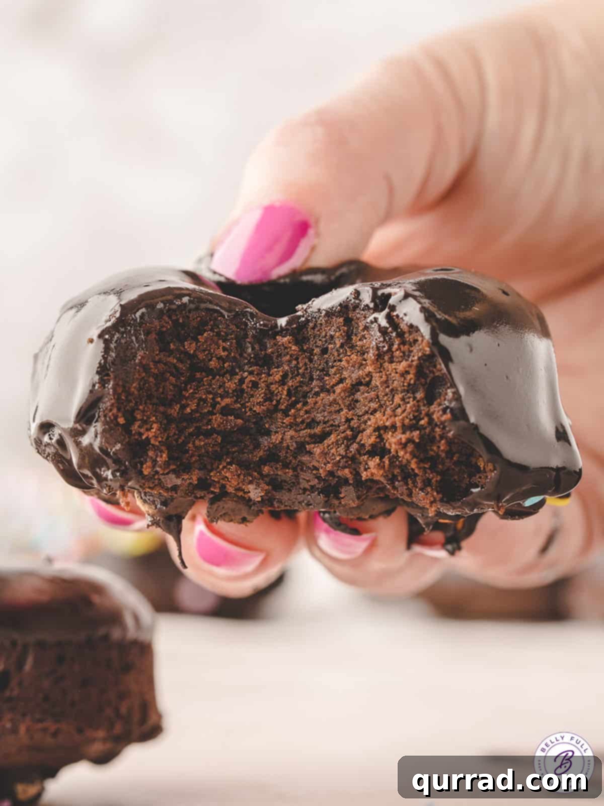 A hand holding a brownie donut, pulled apart to reveal its dense, fudgy interior