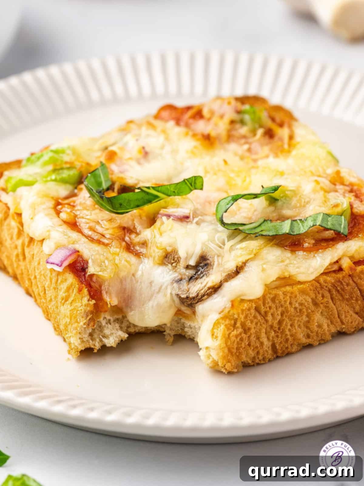 Indulge in a Bite of Pizza Toast A delectable slice of pizza toast on a plate, with a bite taken out, highlighting its cheesy interior and crispy crust.