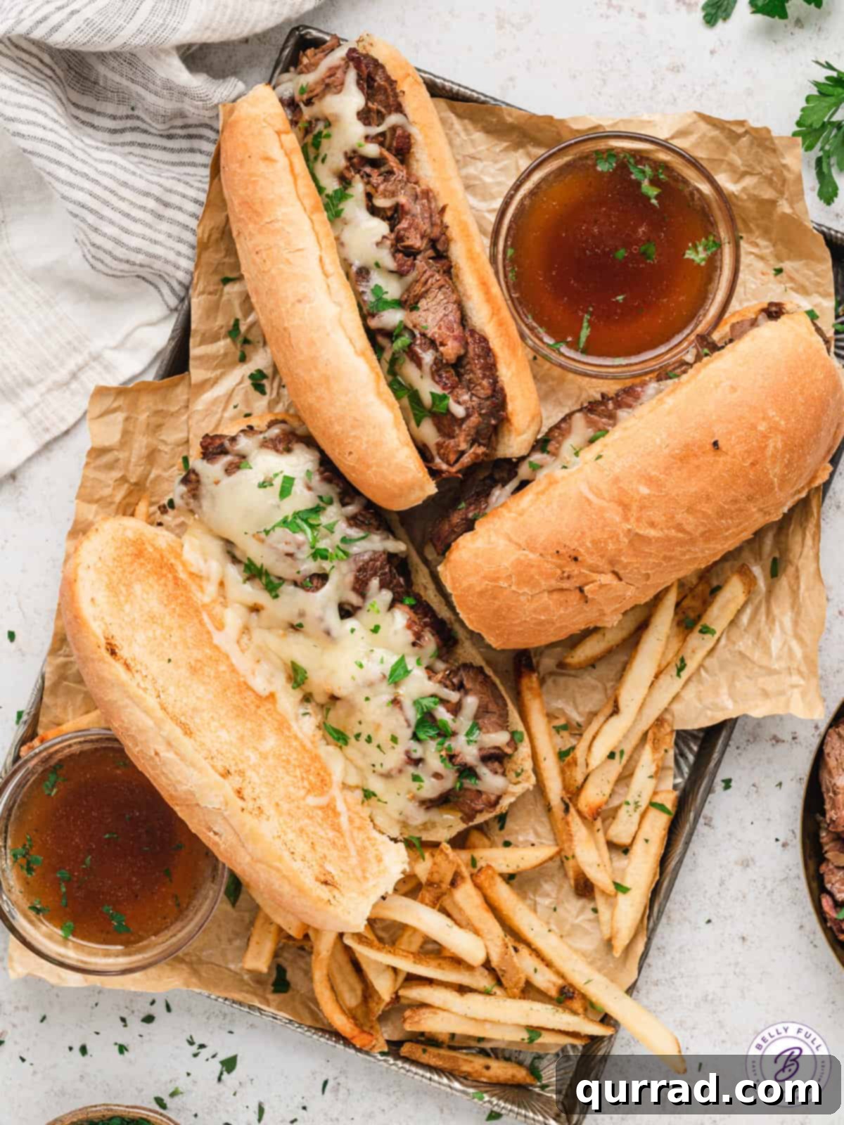 Three perfectly assembled French dip sandwiches, showcasing the tender beef and melted cheese, arranged on a rustic cutting board.