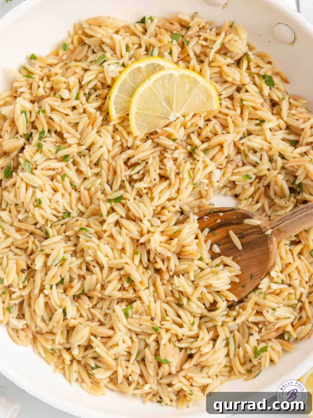 A wooden spoon stirring lemon orzo with fresh parsley on top