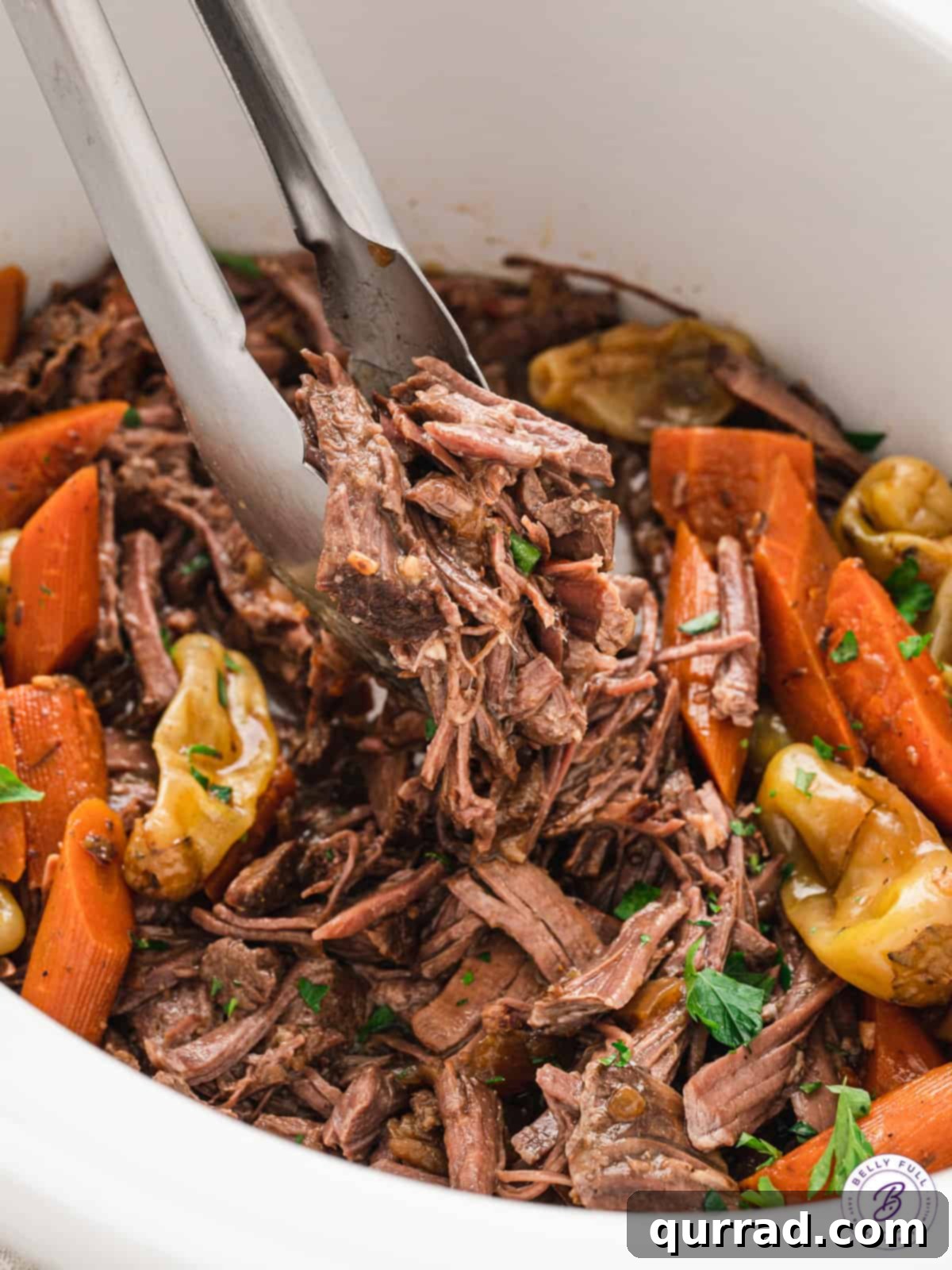 Southern Comfort Mississippi Pot Roast 8 A close-up of shredded Mississippi Pot Roast being served with tongs from a slow cooker, showcasing its tender texture.