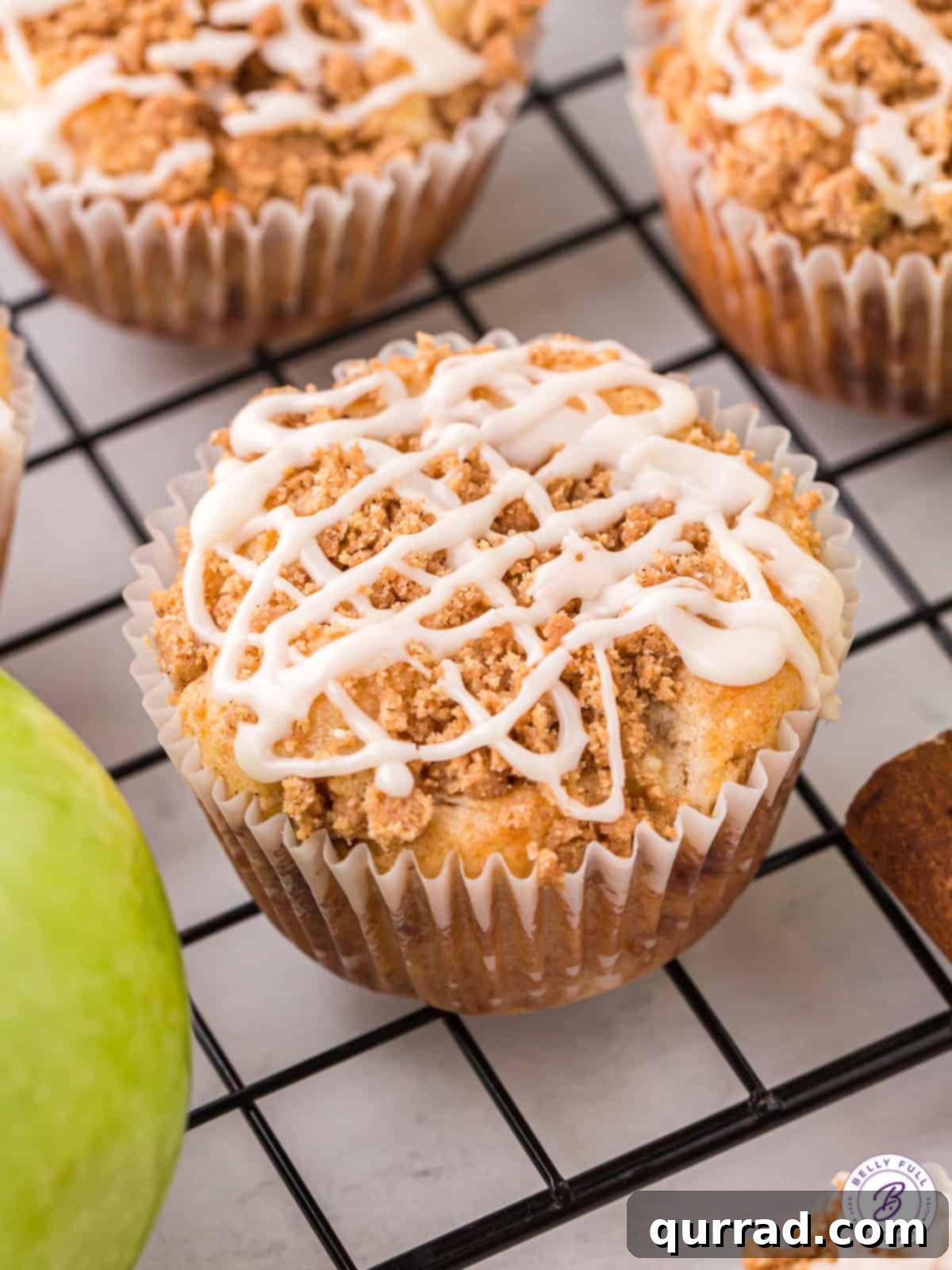 Spiced Apple Crumble Muffins 9 A beautifully baked apple streusel muffin adorned with a sweet vanilla glaze drizzled over its golden streusel topping, ready to be enjoyed.