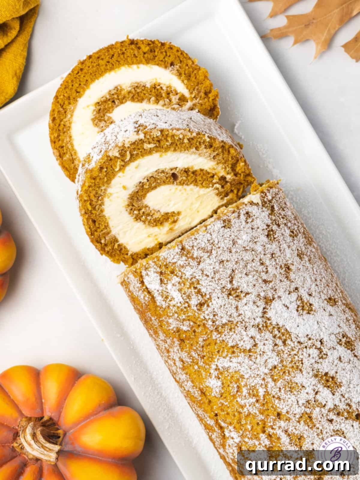 Overhead view of a beautifully sliced pumpkin roll cake, revealing the perfect spiral of pumpkin cake and cream cheese filling. Two pieces are already served.