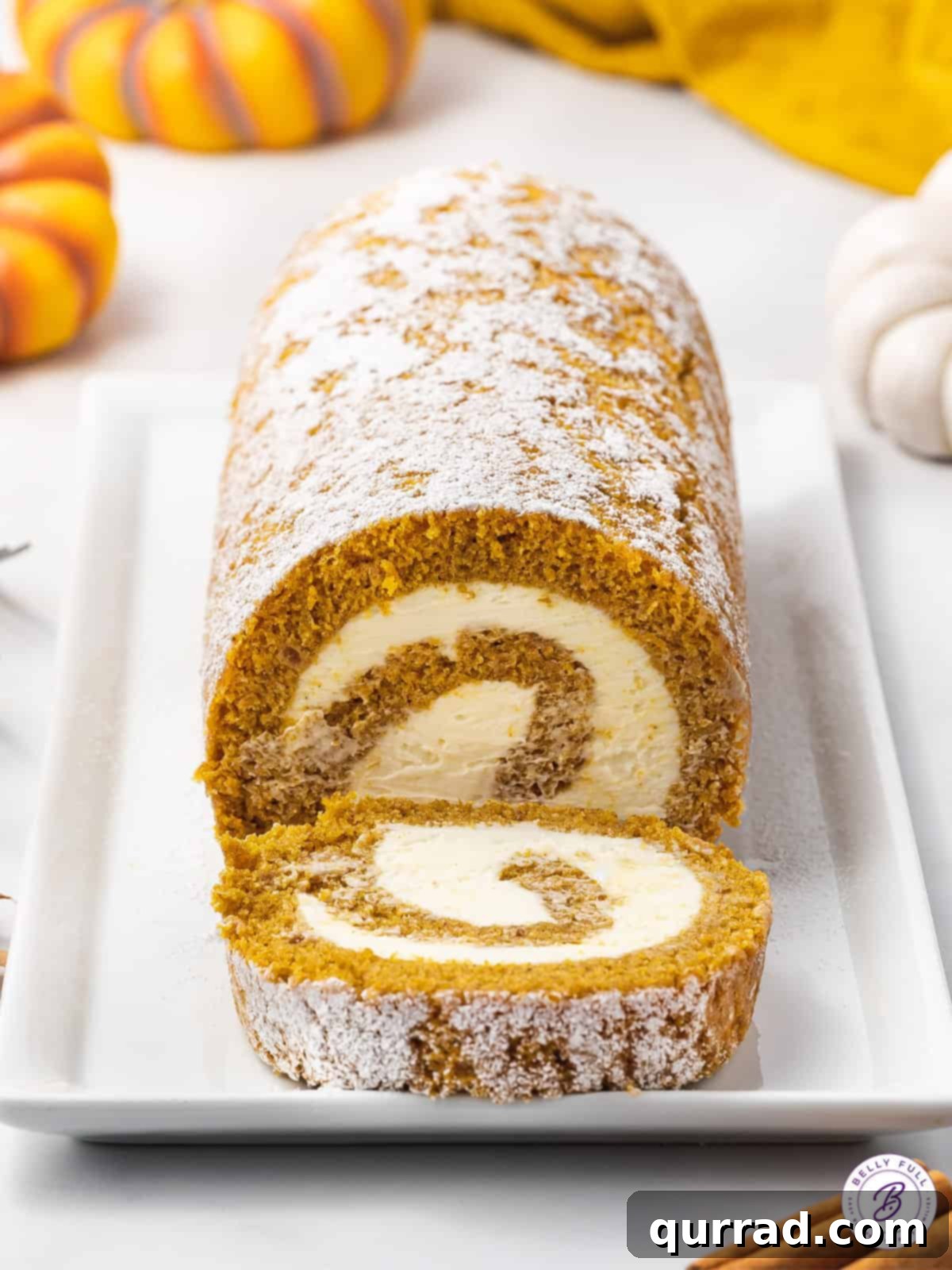 Front view of a perfectly rolled pumpkin cake with a generous layer of cream cheese frosting, with one slice cut and served on a plate, ready to be enjoyed.