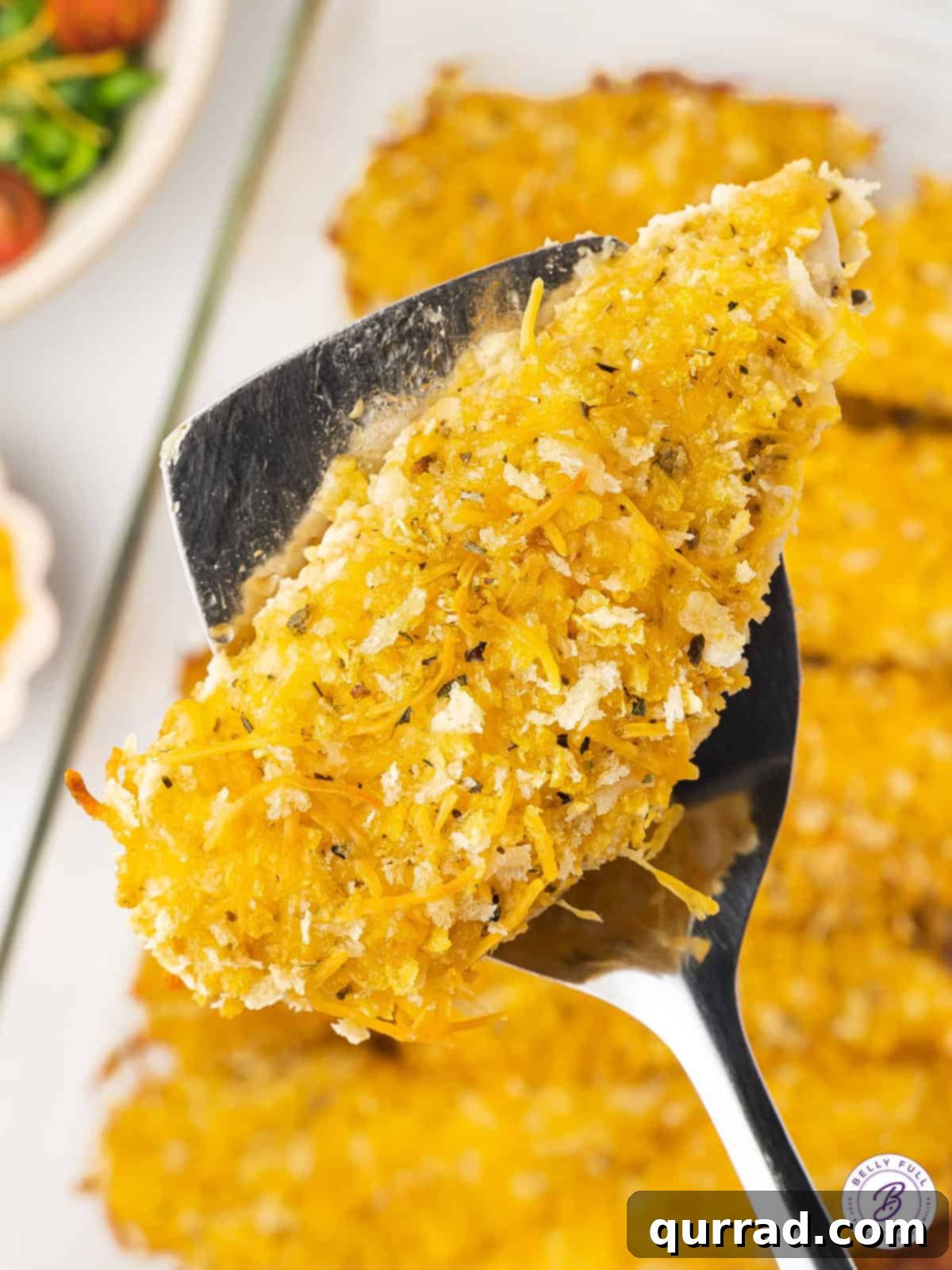 A cheddar baked chicken tender on a spatula, showcasing its golden, crispy, and cheesy crust