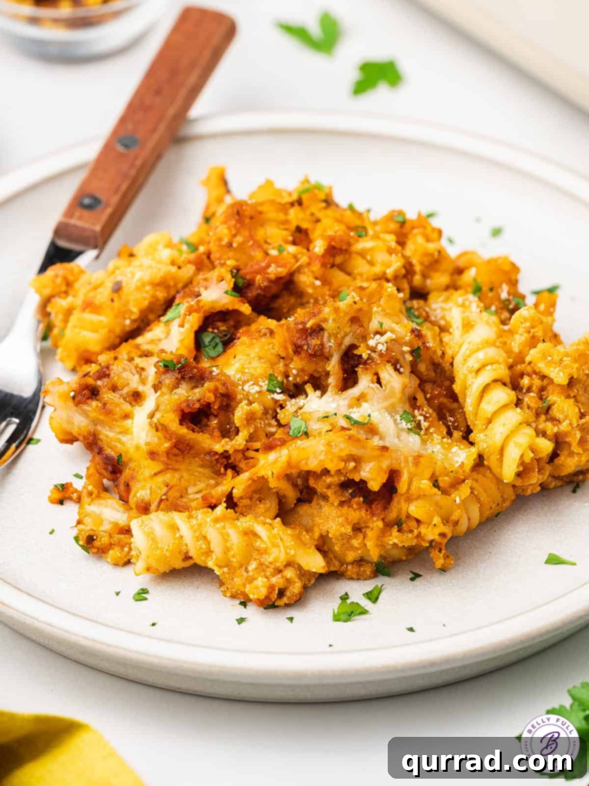 Individual serving of cheesy Chicken Parmesan Casserole A serving of parmesan chicken casserole on a plate, garnished with fresh herbs