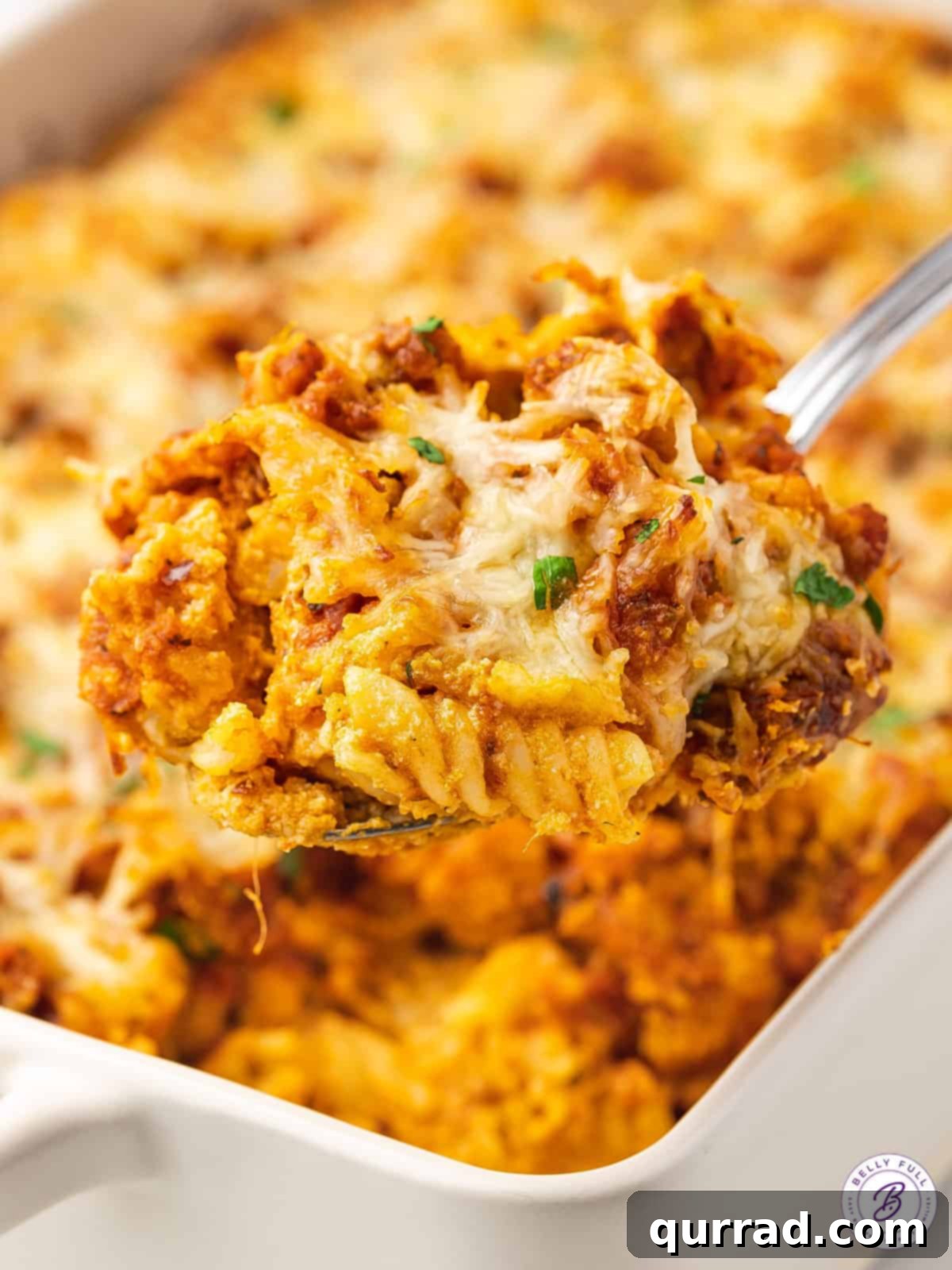Serving a hearty portion of Chicken Parmesan Casserole A spoon scooping a portion of Chicken Parmesan Casserole from the dish