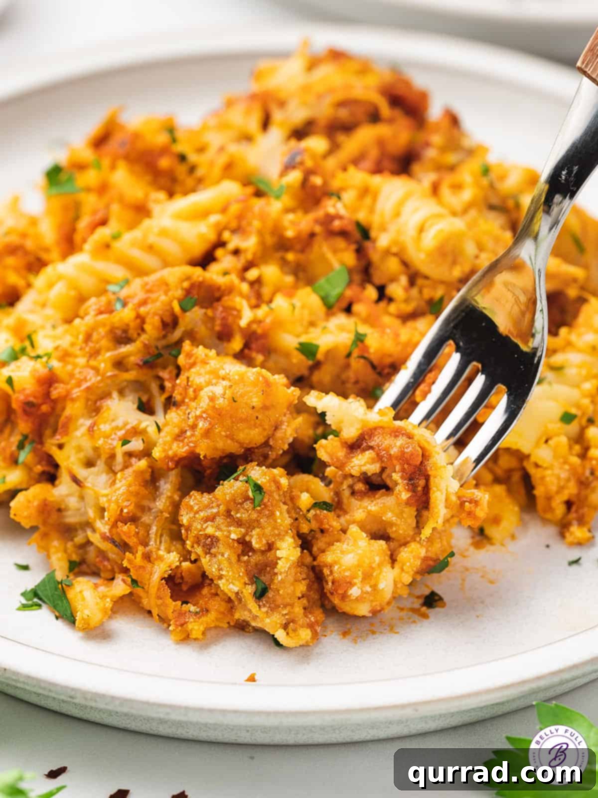 A forkful of savory Chicken Parmesan Casserole A fork taking a bite of Chicken Parmesan Casserole from a plate