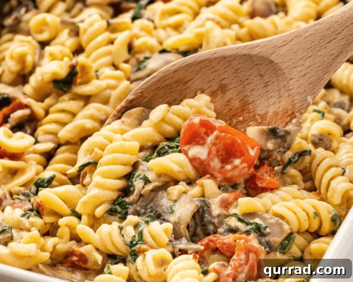 Based on the viral TikTok recipe, Baked Boursin Pasta is made with rotini, veggies, and garlic and herb Boursin cheese. Ready in 35 minutes! A wooden spoon serving Boursin cheese pasta from a large baking dish.