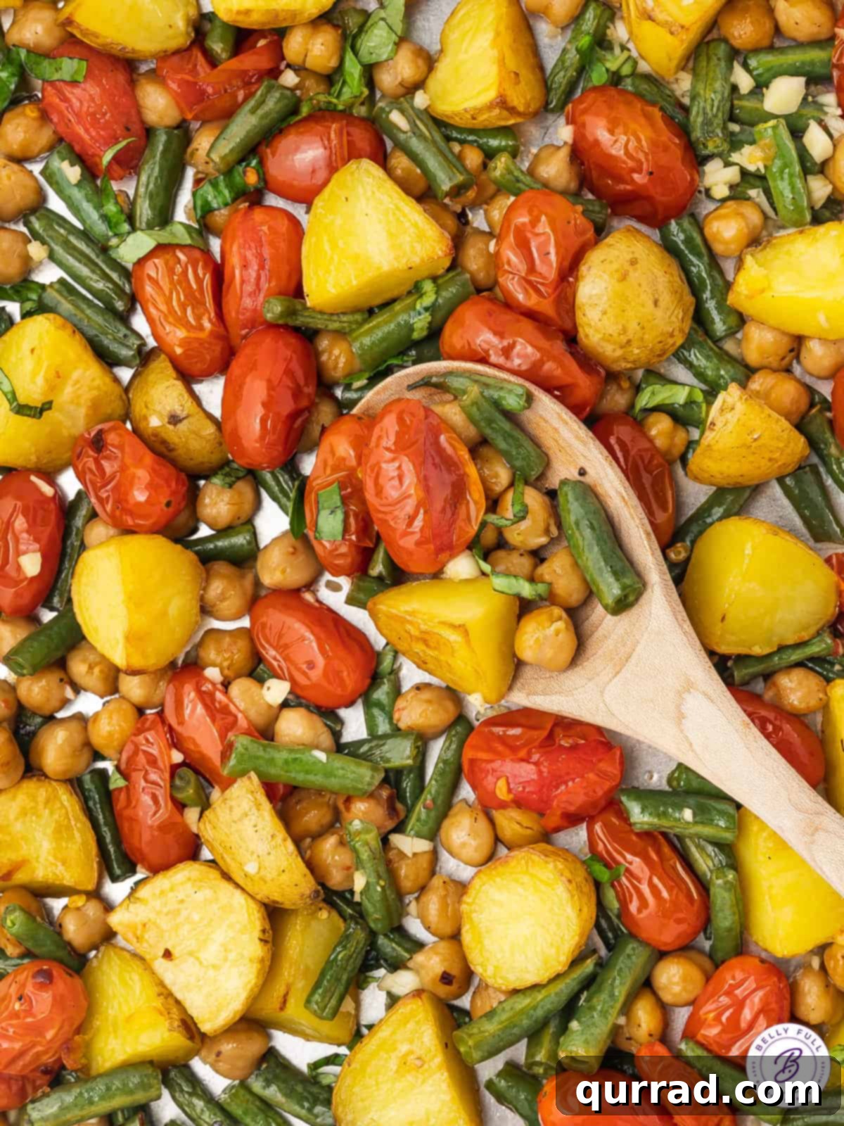 A wooden spoon gently stirring a vibrant assortment of roasted vegetables and chickpeas on a sheet pan, showcasing the deliciousness of a homemade vegan sheet pan dinner.
