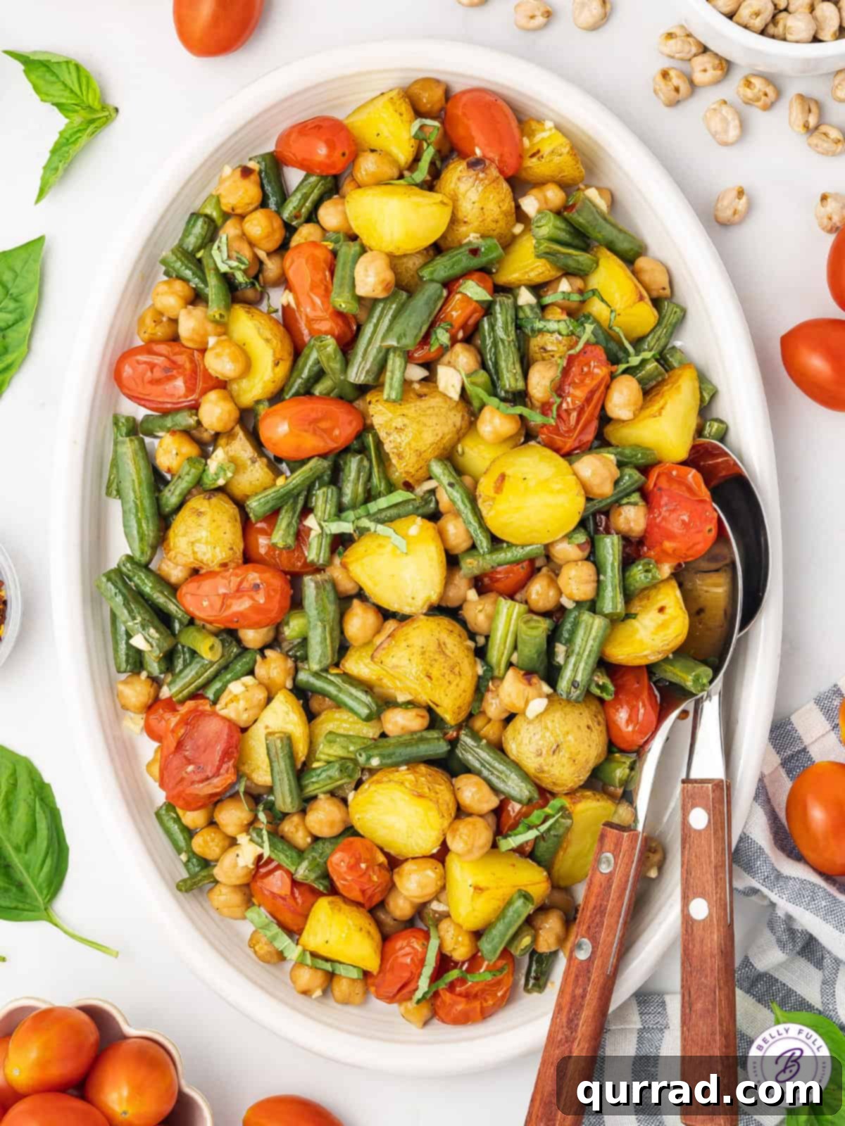 A beautifully arranged serving of vegetarian sheet pan dinner on a white platter, featuring golden-brown potatoes, bright green beans, burst tomatoes, and crispy chickpeas.