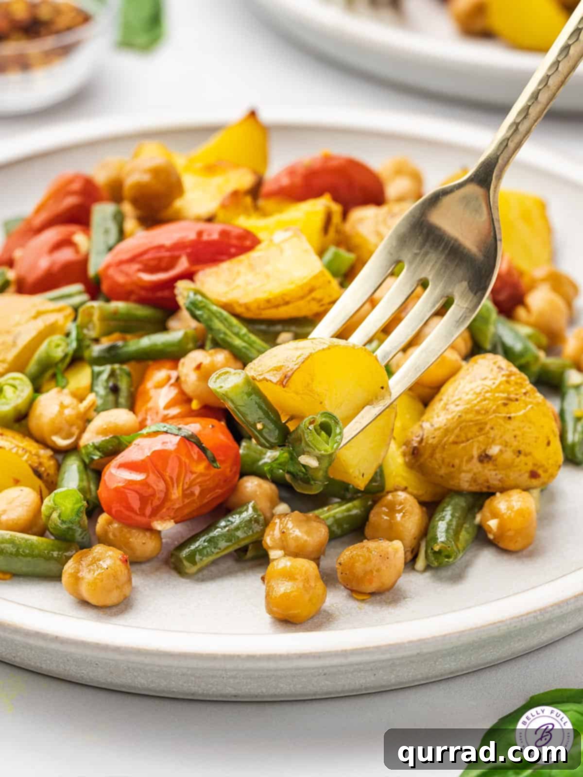 A fork piercing a piece of perfectly roasted potato, highlighting the tender interior and golden-brown exterior of the vegan sheet pan dinner.