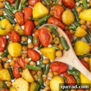 A wooden spoon stirring a veggie sheet pan dinner