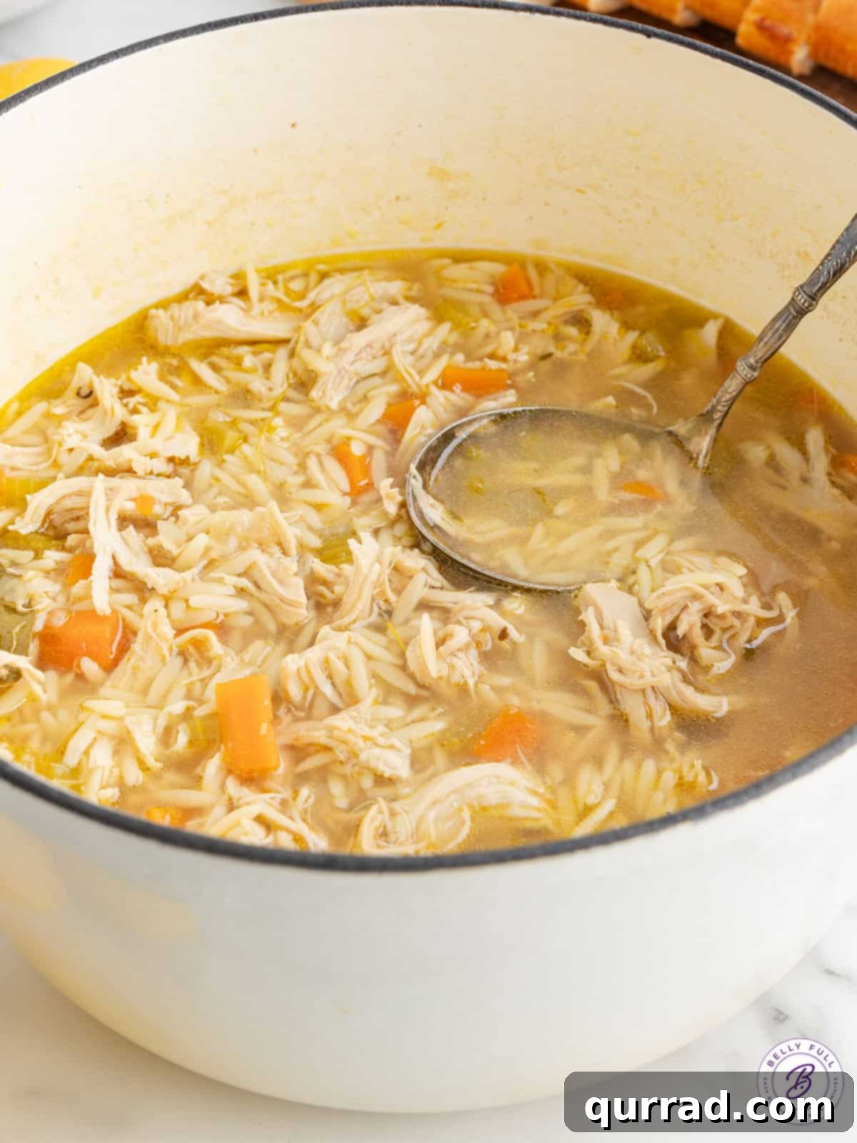 Zesty Lemon Chicken Orzo Soup 4 A ladle scooping hot Lemon Chicken Orzo Soup from a large pot, showing the vibrant broth, chicken, and orzo.