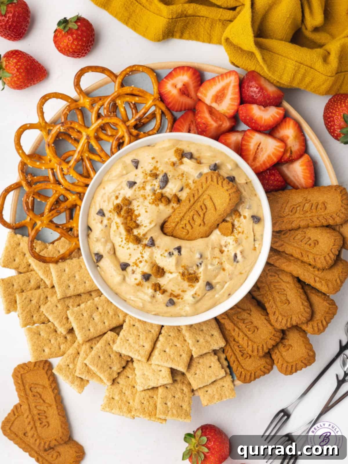 Every bite of this Biscoff Dip is infused with sweet cookie butter flavor! Made with cream cheese, marshmallow fluff, and cookie butter. A vibrant platter showcasing a central bowl of Biscoff dip, elegantly surrounded by a variety of dippers including crunchy pretzels, classic graham crackers, iconic Biscoff cookies, and fresh, juicy strawberries.