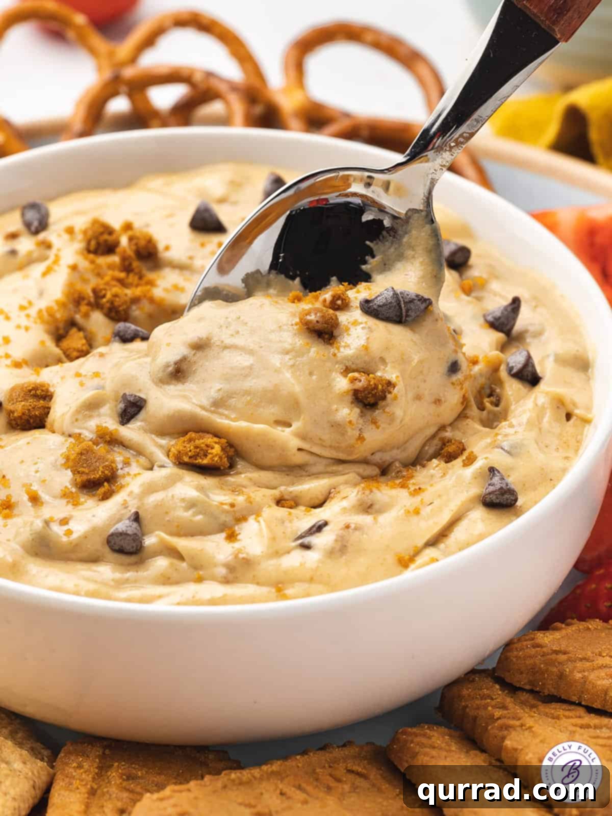 Every bite of this Biscoff Dip is infused with sweet cookie butter flavor! Made with cream cheese, marshmallow fluff, and cookie butter. A silver spoon is gently dipped into a bowl of the rich, creamy Biscoff dip, highlighting its smooth texture and inviting consistency.