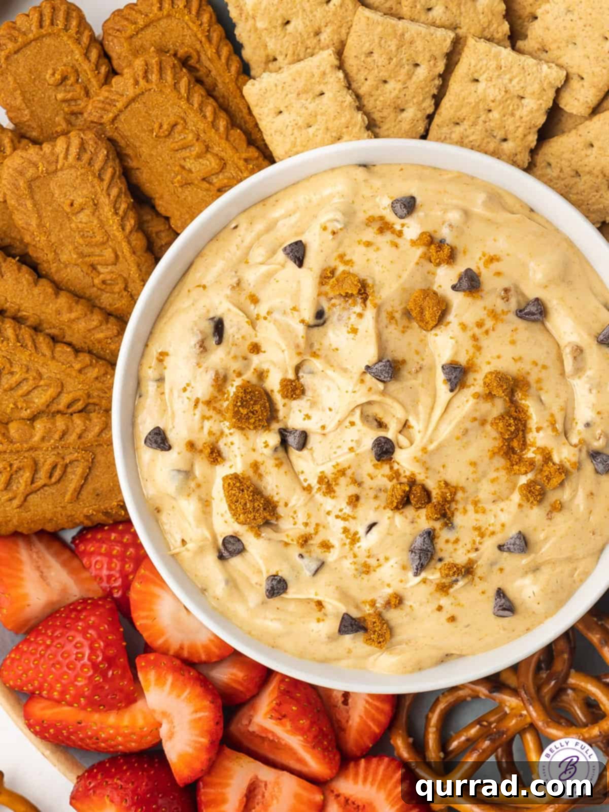 Every bite of this Biscoff Dip is infused with sweet cookie butter flavor! Made with cream cheese, marshmallow fluff, and cookie butter. An inviting overhead view of a generously sized bowl of golden Biscoff dip, artfully arranged on a serving platter and surrounded by a delicious assortment of dippers including Biscoff cookies, crunchy pretzels, and fresh, vibrant strawberries.