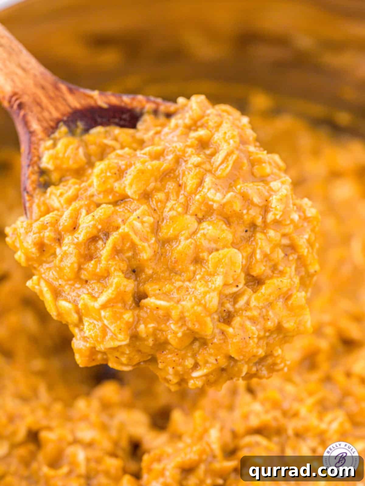 Pumpkin oatmeal is made with wholesome ingredients like oats and pumpkin puree and spiced with warm flavors of pumpkin pie spice, showing the cooking process. A wooden spoon stirring warm pumpkin oatmeal in a saucepan, highlighting the cooking process.