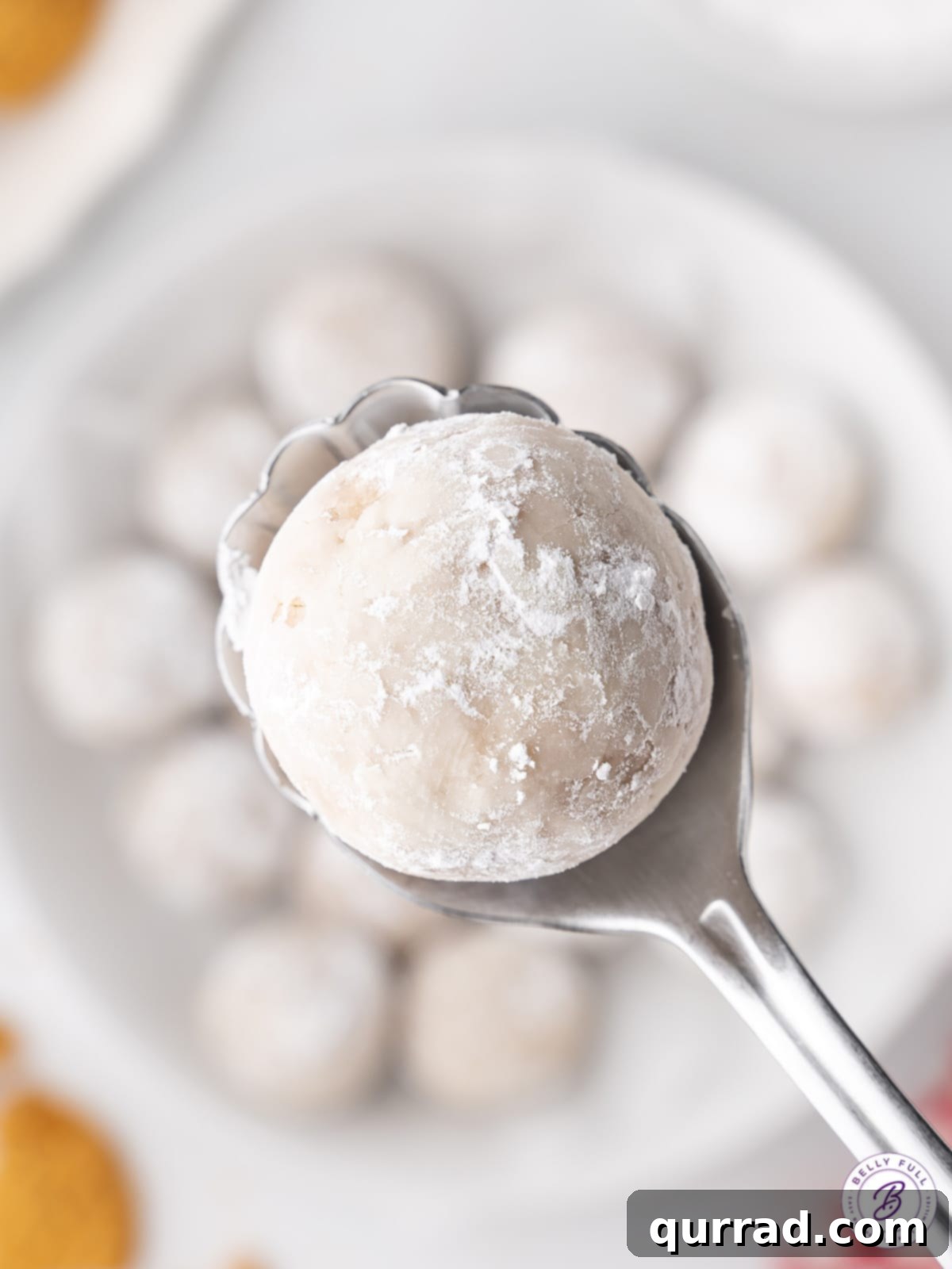 Festive Gingerbread Truffles 4 A close-up, overhead view of a single gingerbread truffle, perfectly coated in powdered sugar, resting on a spoon.