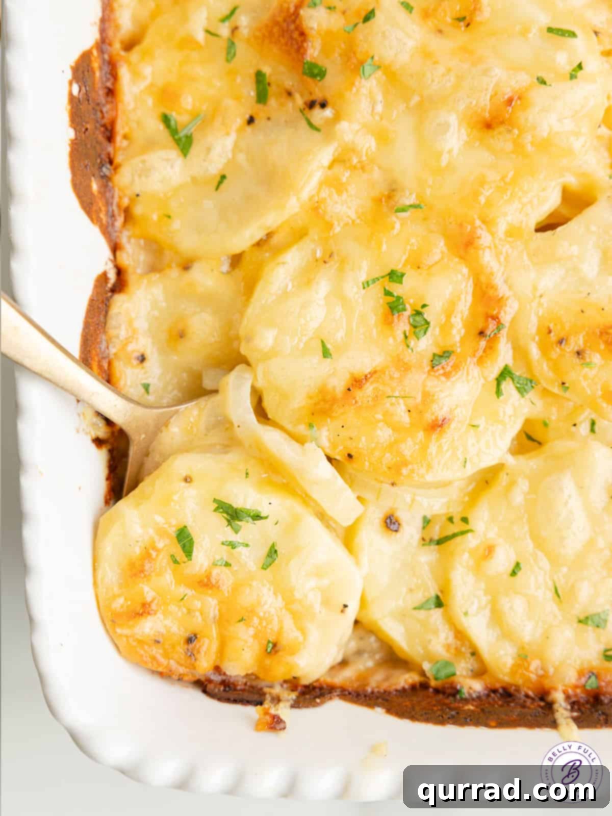 Creamy and Cheesy Au Gratin Potatoes: A Must-Have Side for Any Occasion A spoon scooping creamy au gratin potatoes from a casserole dish, showing layers of thinly sliced potatoes and melted cheese.