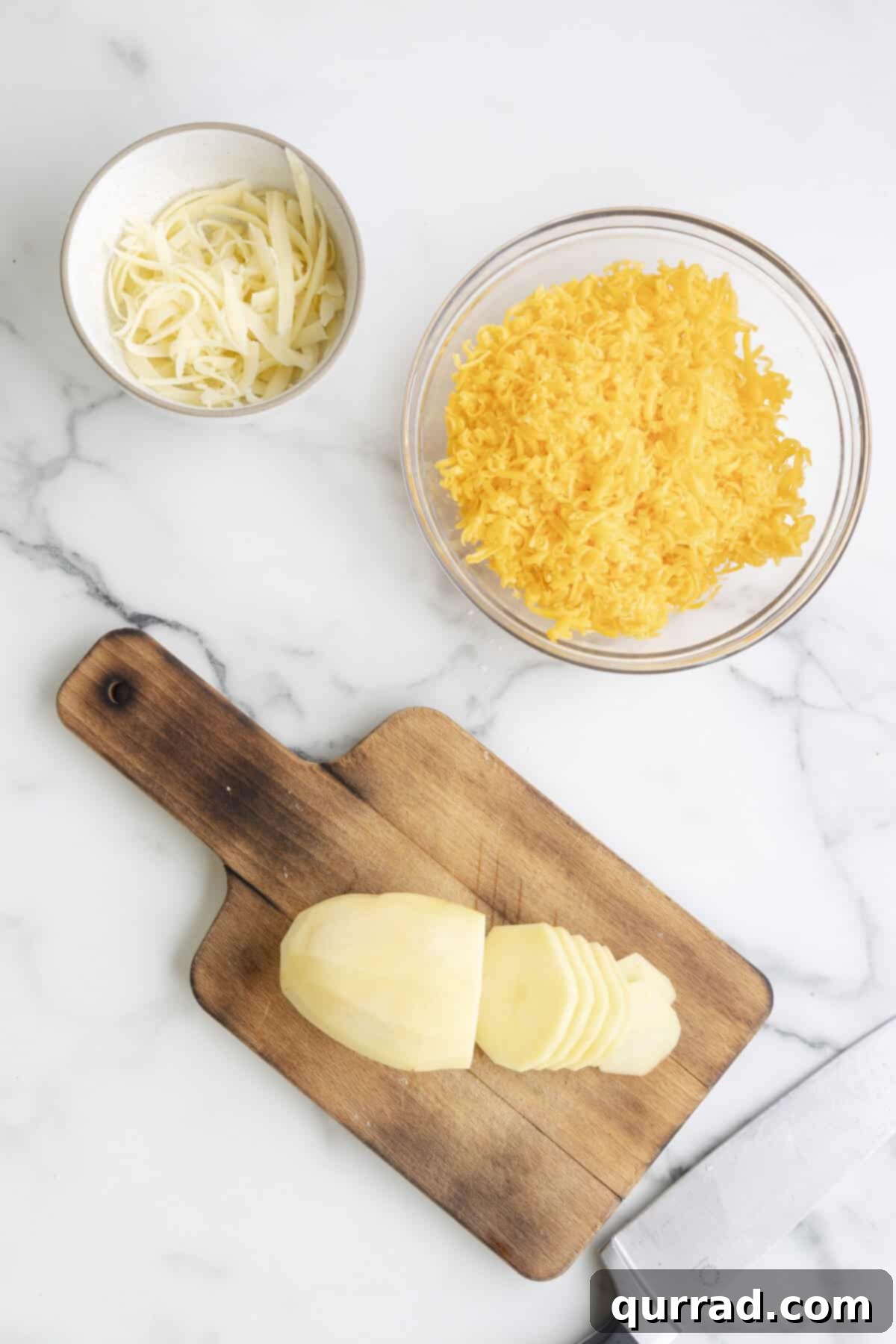 Au Gratin Potatoes 4 A mandoline slicer being used to thinly slice a russet potato on a wooden cutting board, producing even, uniform potato rounds.