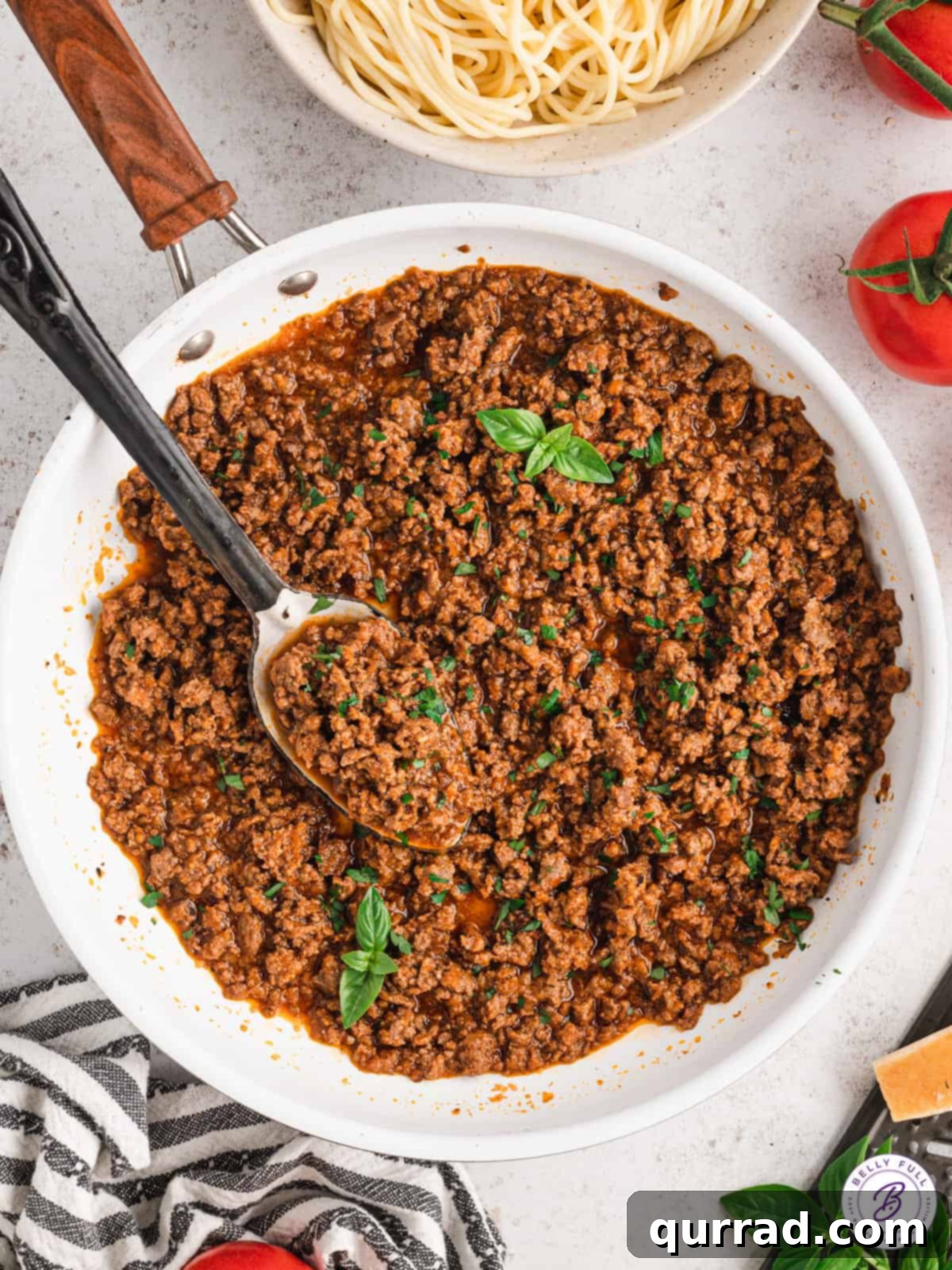 Observe the rich consistency of Magic Meat Sauce as it's stirred, promising deliciousness. A large white bowl of rich, simmering meat sauce being stirred with a spoon, highlighting its thick texture and vibrant color.