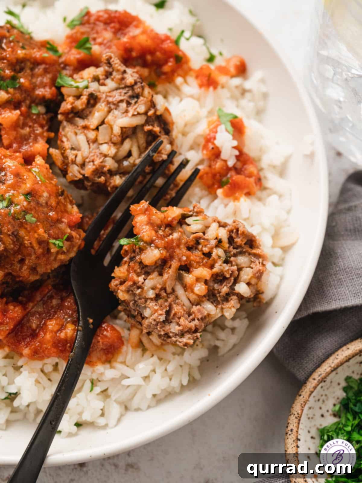 A black fork next to a porcupine meatball cut in half on a plate of rice, showing the internal texture