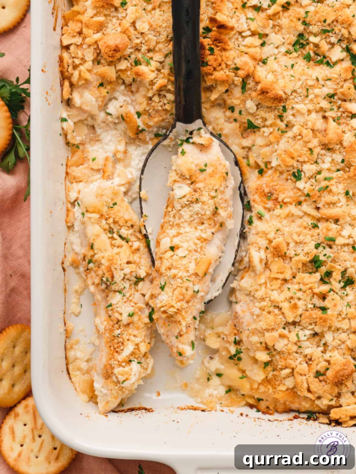 A serving spoon lifting a generous portion of creamy Ritz Cracker Chicken from a casserole dish, highlighting the tender chicken and crispy topping.