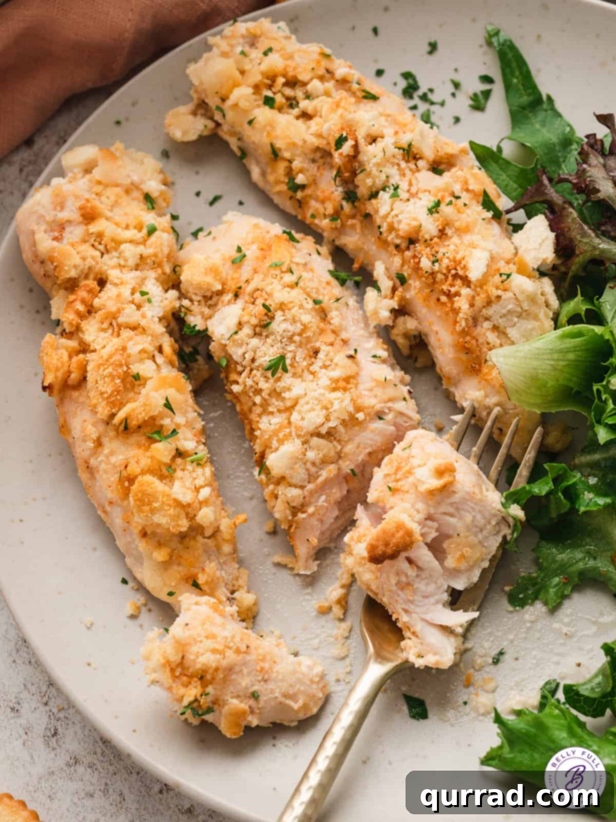 Three pieces of golden-brown Ritz Cracker Chicken served on a white plate alongside a vibrant green salad, showcasing a balanced and appealing meal.