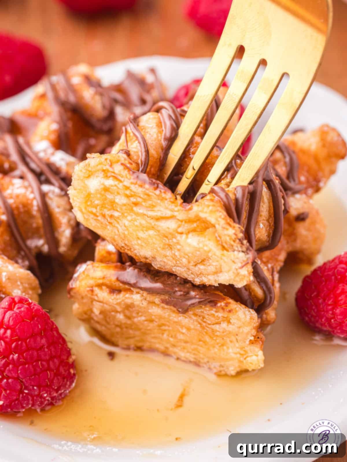 A fork piercing a golden-brown croffle, revealing its flaky layers, with a generous drizzle of maple syrup adding to its allure.