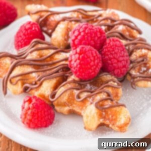 Two golden-brown croffles on a white plate, drizzled with chocolate sauce and adorned with fresh berries, for the recipe card.