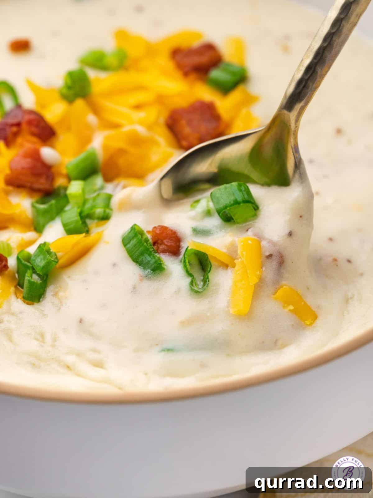 Copycat Panera Baked Potato Soup is rich, creamy, and full of incredible flavor, thanks to ingredients like cream cheese and bacon. A spoon resting in a full bowl of baked potato soup, showing the creamy texture and inviting toppings.