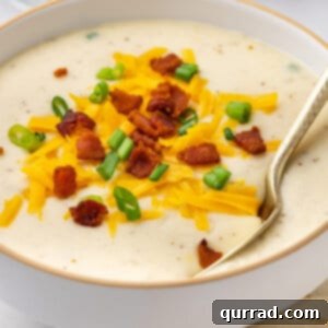 Angled view of a bowl of Panera baked potato soup topped with cheese, bacon, and scallions