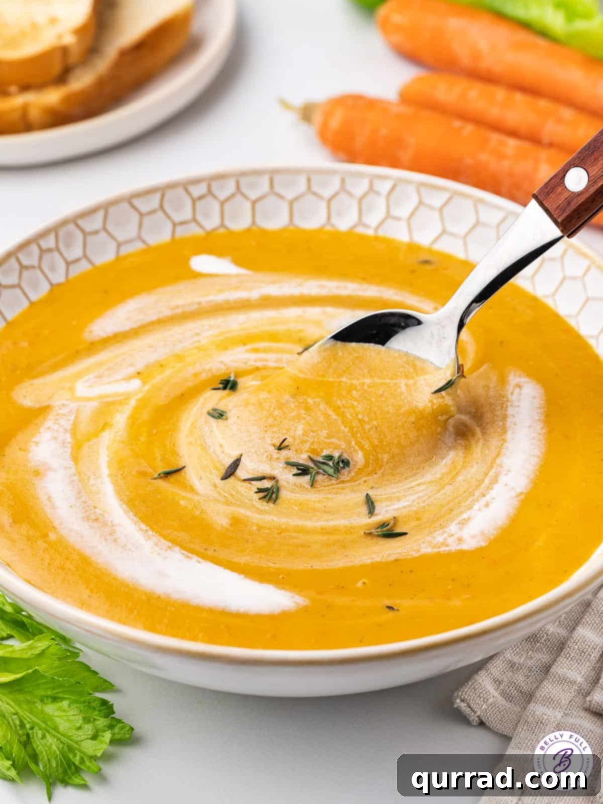 A spoon in a bowl of creamy carrot soup, garnished with a swirl of cream and fresh herbs.