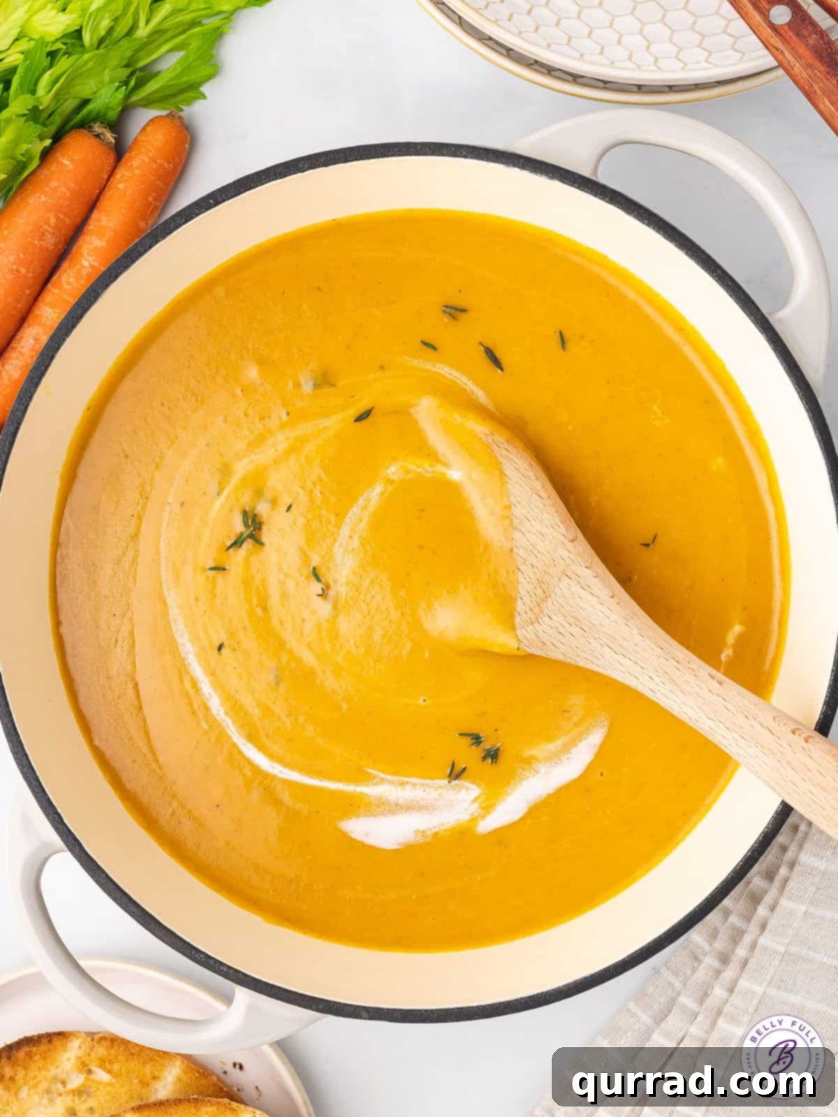 A wooden spoon gently stirring a pot of creamy carrot soup, ready for serving.