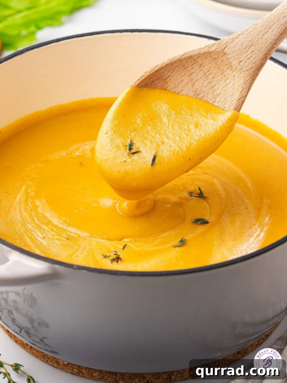 A wooden spoon resting in a pot of golden, creamy carrot soup, indicating it's ready.