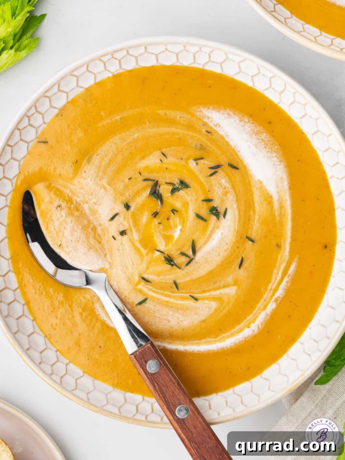 A spoon swirling cream into a bowl of perfectly garnished creamy carrot soup, ready to be enjoyed.
