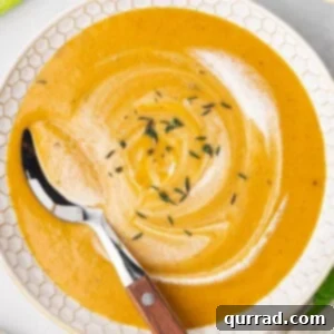 A spoon swirling cream in a bowl of carrot soup, ready to be served.