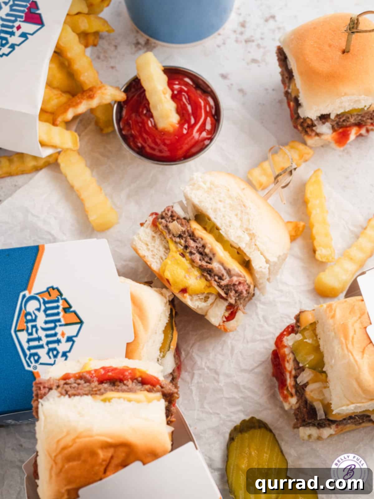 With thin beef patties topped with American cheese on slider buns, these White Castle Burgers are quick, easy, and family-approved. An appetizing close-up of a White Castle slider, garnished with a dill pickle and onions, served alongside a pile of golden, crispy french fries.