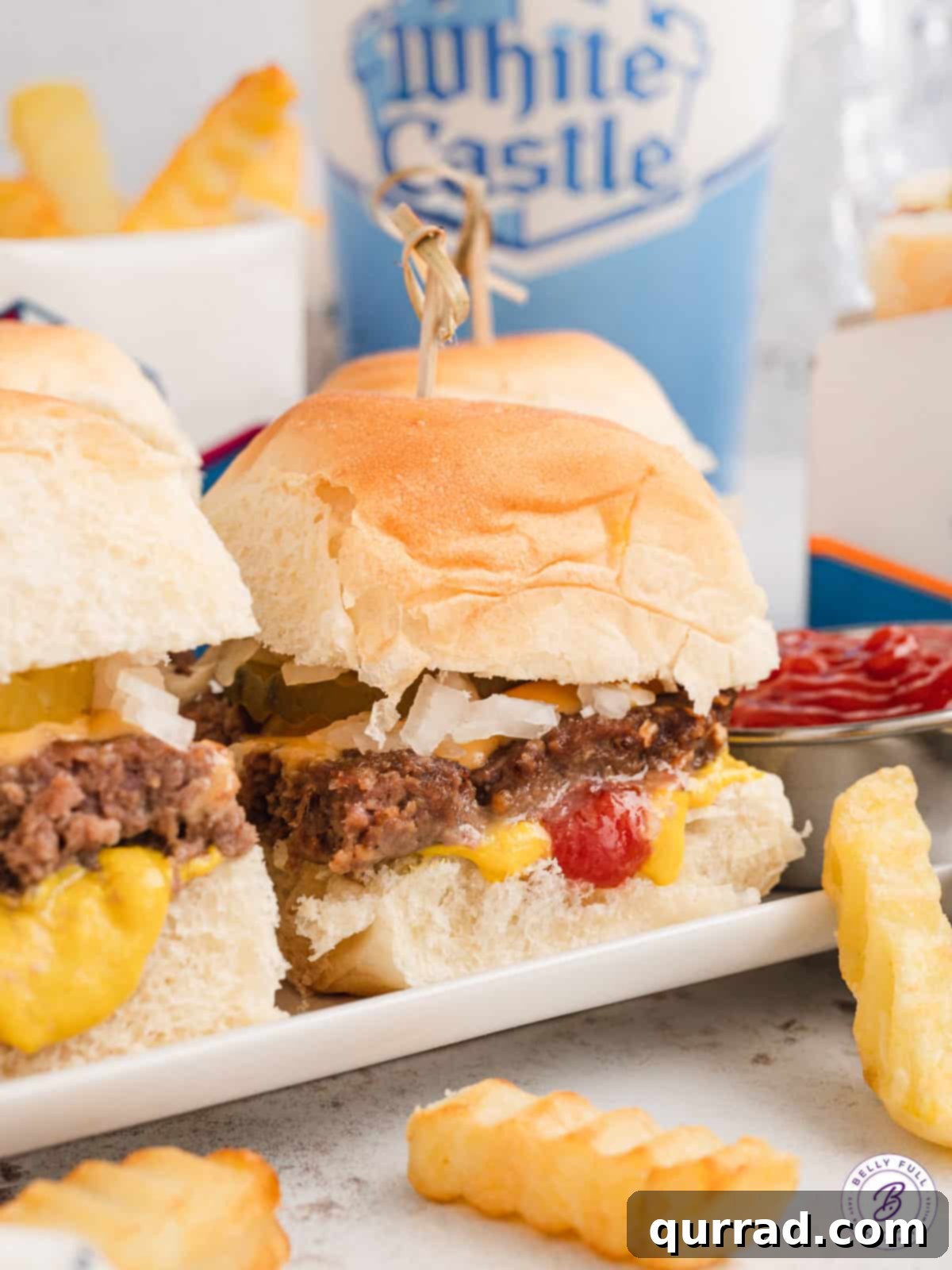 With thin beef patties topped with American cheese on slider buns, these White Castle Burgers are quick, easy, and family-approved. A delightful arrangement of White Castle sliders on a pristine white plate, accompanied by a generous serving of crispy golden fries, inviting immediate enjoyment.