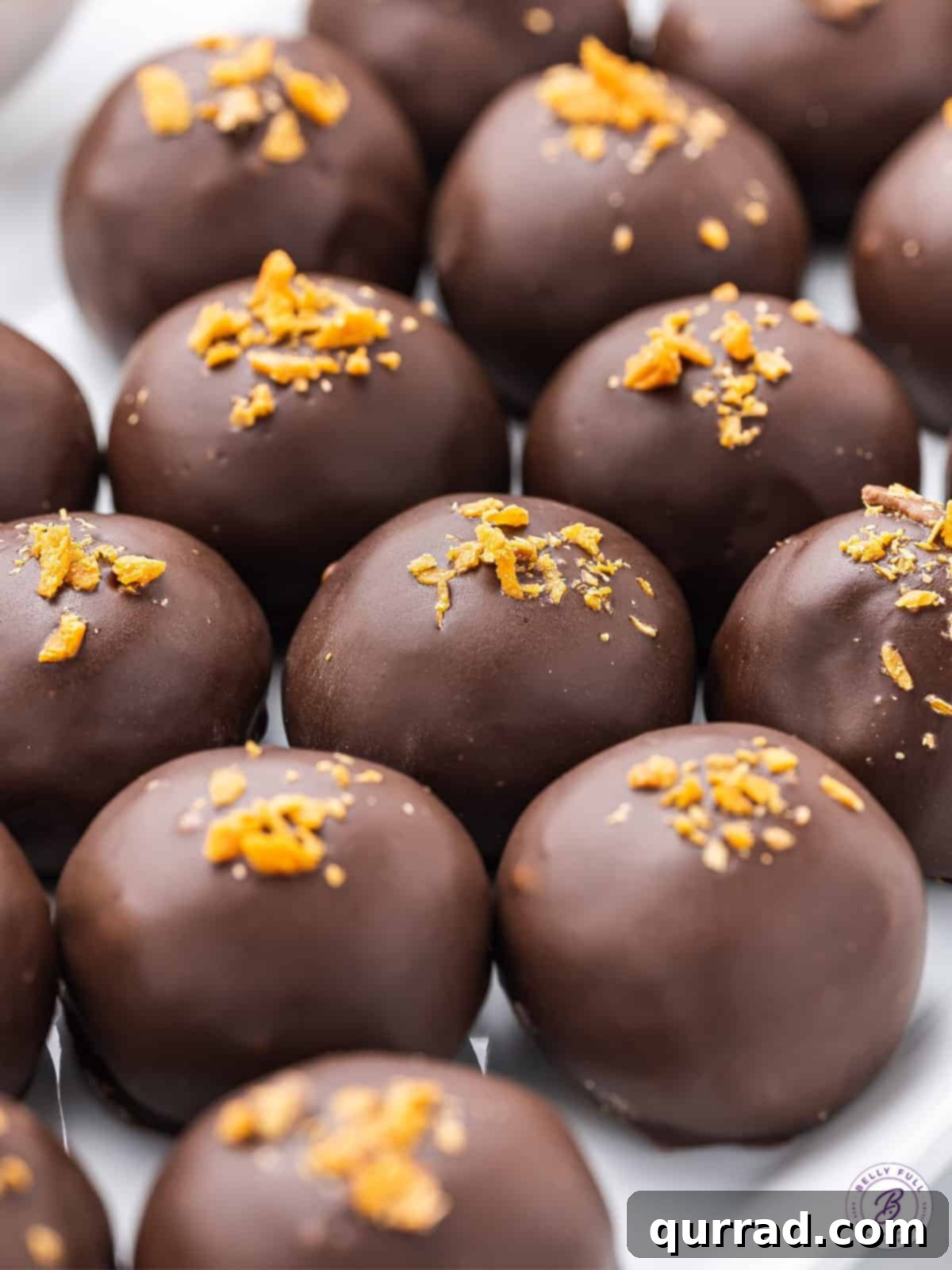 A close-up view of a perfectly dipped Butterfinger Truffle adorned with delicate crumbs of the candy bar, showcasing the rich chocolate and crispy topping.