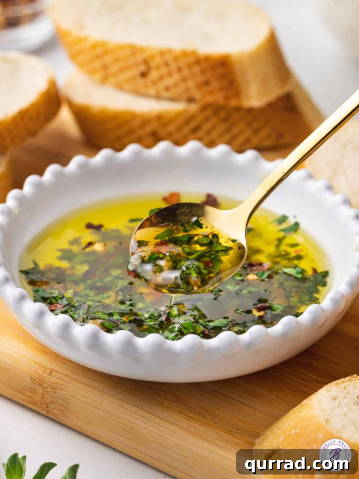 A close-up shot of a spoon gracefully scooping up rich, herbed olive oil from a shallow ceramic bowl, showcasing the vibrant green flecks of fresh herbs and the golden hue of the oil.