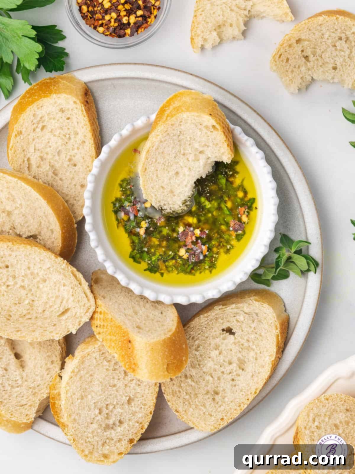 An overhead view of a wooden cutting board with a freshly sliced loaf of crusty Italian bread, strategically arranged around a small white bowl brimming with homemade bread dipping oil, ready for a delicious appetizer.